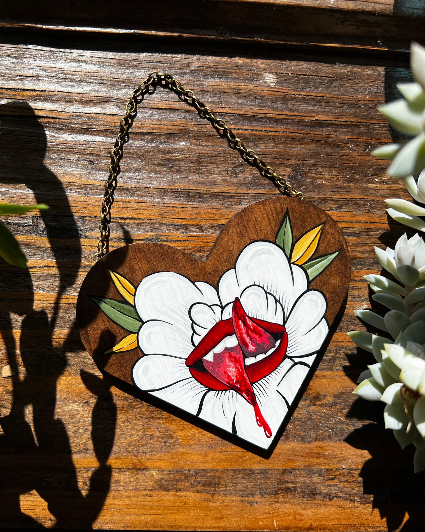 A painting on a small wooden heart of a split tongue coming out of a white flower 