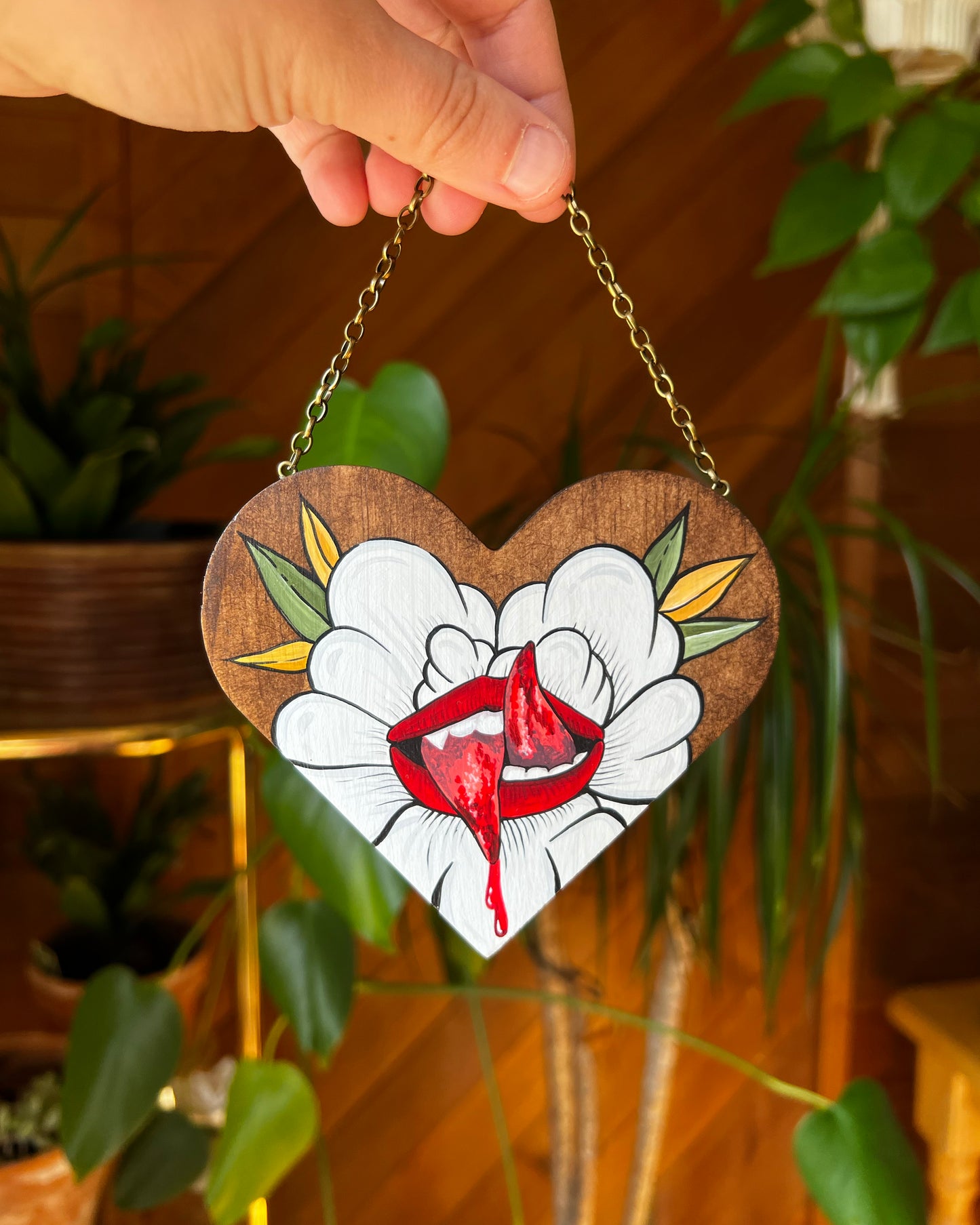 A painting on a small wooden heart of a split tongue coming out of a white flower 