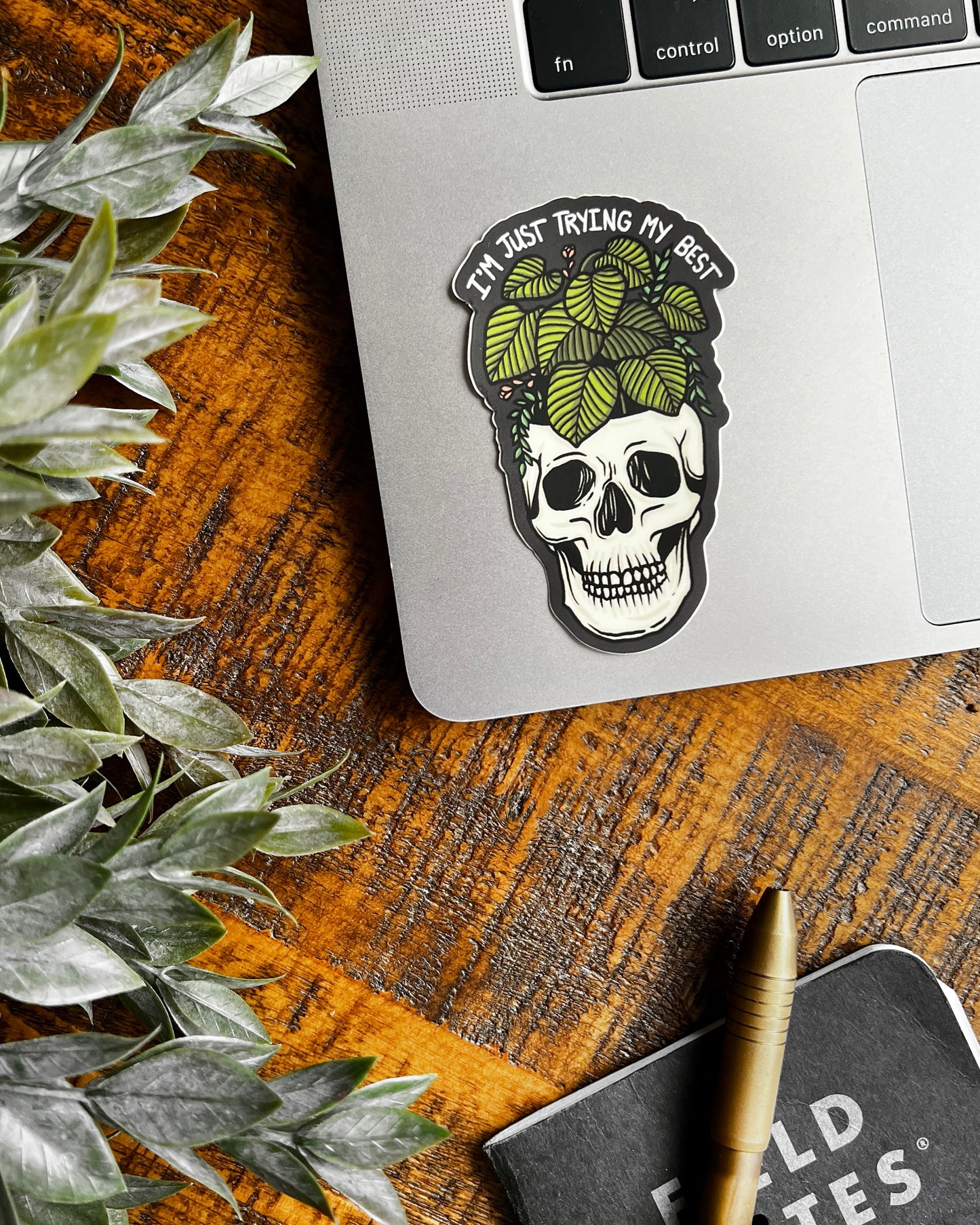 Skull sticker with leaves and text 'I'm just trying my best' on a gray background on a laptop